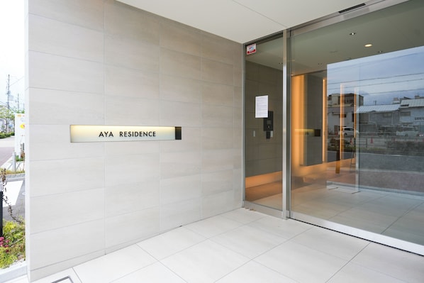 Une entrée moderne avec une enseigne indiquant « RÉSIDENCE AYA » et une porte vitrée donnant accès à l’intérieur.