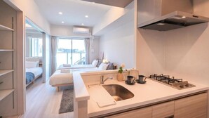 A modern hotel room with a kitchenette, a bed, a large window, and a view of the city. - AYA RESIDENCE (Osaka)