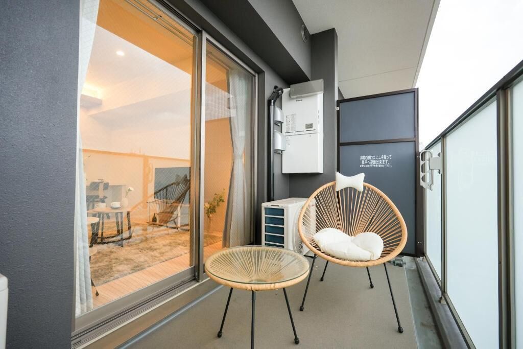A balcony with two wicker chairs, a small table, and a refrigerator.