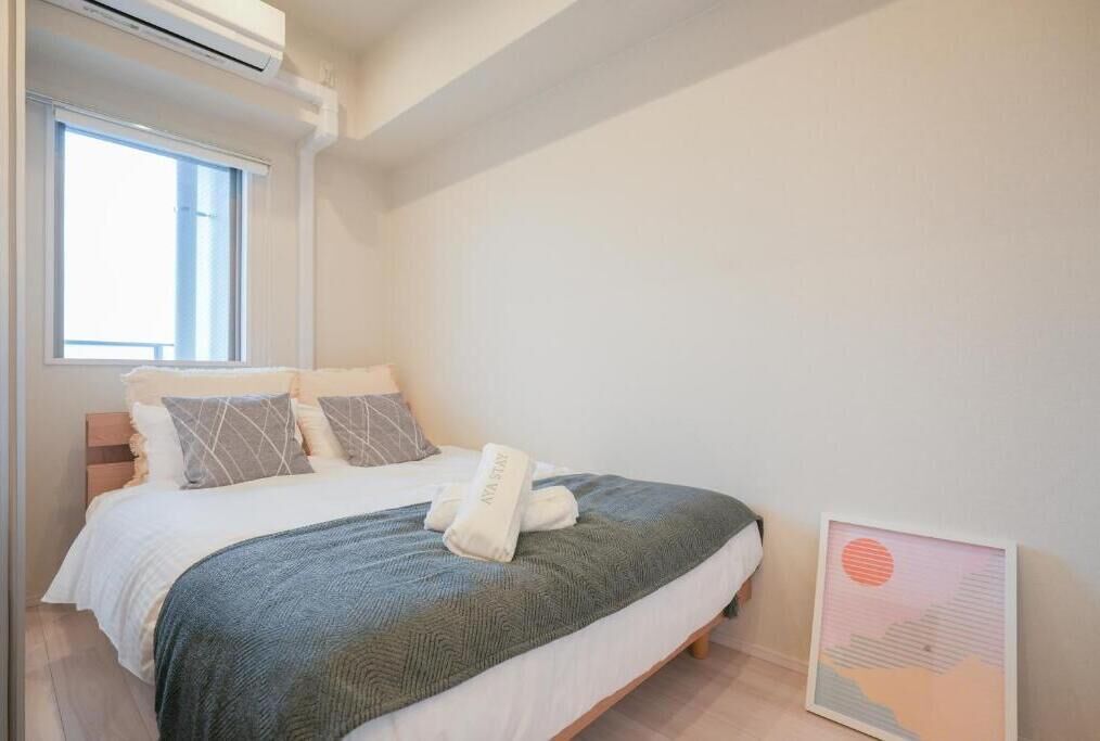 A bedroom with a bed, pillows, a blanket, a framed picture, and a window.