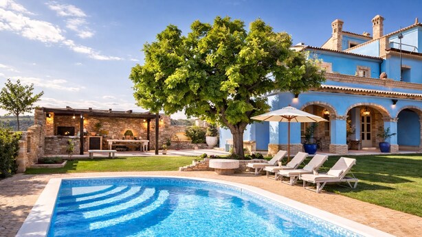 A pool with lounge chairs, a pergola, and a stone building with arches.