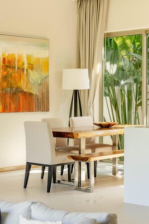 Een moderne eethoek met een houten tafel, witte stoelen, een vloerlamp en een groot abstract schilderij aan de muur.