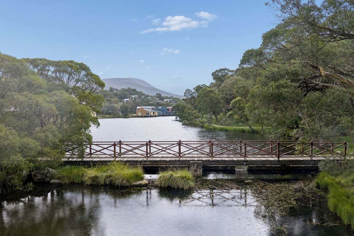 Eine Holzbrücke über einem ruhigen Fluss, umgeben von Grün und mit einem entfernten Berg.