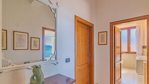 A hallway with a wooden door, a mirror, and a fish-shaped vase on a console table. - Residenza Bellavista - Bianco (Capoliveri)