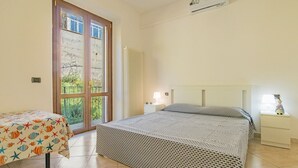 A bedroom with two beds, a window with a view, a radiator, and a small table with a lamp. - Residenza Bellavista - Bianco (Capoliveri)