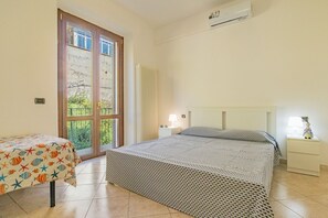 A bedroom with two beds, a window with a view, a radiator, and a small table with a lamp. - Residenza Bellavista - Bianco (Capoliveri)