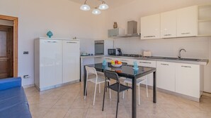 A compact kitchen with a dining area, white cabinets, a refrigerator, a microwave, and a gas stove. - Residenza Bellavista - Bianco (Capoliveri)