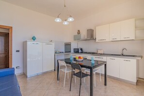 A compact kitchen with a dining area, white cabinets, a refrigerator, a microwave, and a gas stove. - Residenza Bellavista - Bianco (Capoliveri)