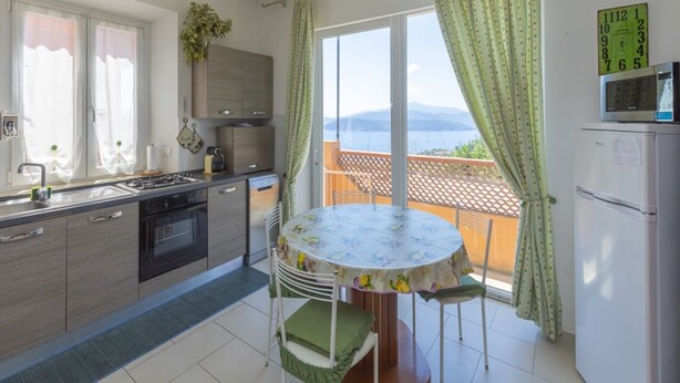 Cozinha com mesa e cadeiras, vista para o mar e varanda.