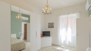 Um quarto com cama, televisão, lustre, espelho e porta.