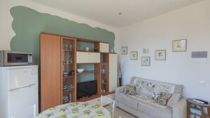 Espaço compacto com cozinha compacta, sofá, mesa de jantar e armário com prateleiras.
