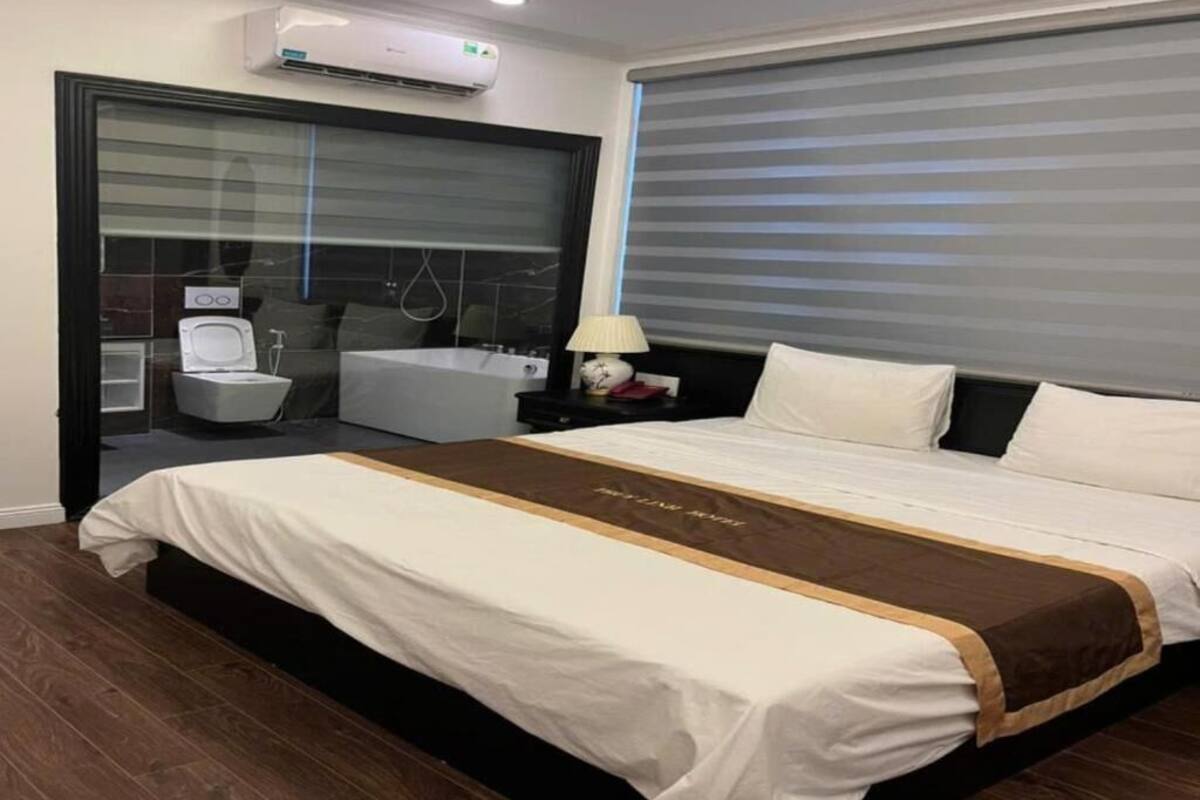 A hotel room with a large bed, a bathroom with a bathtub, and a window with blinds.