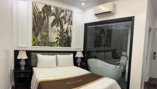Ein Schlafzimmer mit einem Bett, einem Nachttisch, einer Lampe, einem großen Gemälde, einer Badewanne und einer Klimaanlage.
