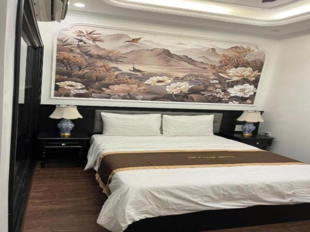 Habitación de hotel con una cama grande, dos mesitas de noche, un cuadro colgado en la pared y suelo de madera.
