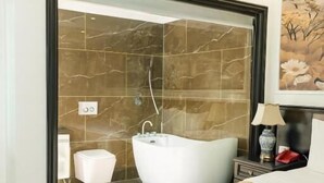 Ein Schlafzimmer mit Bett, Nachttisch, Lampe, Wandklimaanlage und einem Badezimmer mit Badewanne und Dusche.