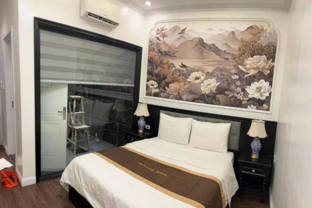 A hotel room with a bed, a nightstand, a lamp, a painting on the wall, and a sliding door.