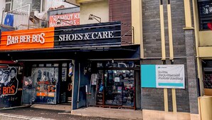 Fachada con letreros que dicen 'Barber Bos' y 'Zapatos y Cuidado'.