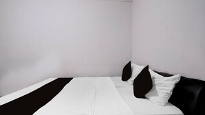 Una cama individual con cubrecama blanco y almohadillas negras, cabecera negra y pared blanca lisa.