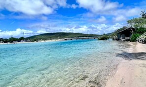 A beach with clear water, a wooden structure, and a bridge in the background. - Haven at Hastings (Tweed)
