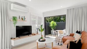 A modern living room with a TV, sofa, coffee table, and a view of the outdoor patio. - Haven at Hastings (Tweed)