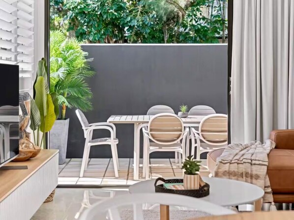 A modern living room with a sofa, a coffee table, and a dining area with chairs and a table. - Haven at Hastings (Tweed)