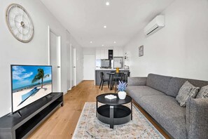 A modern living room with a flat-screen TV, a sofa, a coffee table, and a kitchen in the background. - Central Southbank Apartment with Pool Access (Southbank)