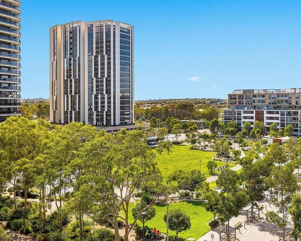 A high-rise building with a modern design, surrounded by a well-maintained park with trees and pathways.