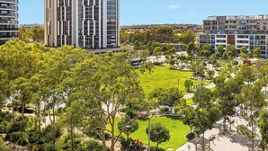 A high-rise building with a modern design, surrounded by a well-maintained park with trees and pathways. - New 2 bedroom apartment. Garden view with pool, jacuzzi,sauna & gym. (Eastgardens)