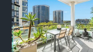A balcony with a table and chairs, potted plants, and a statue. - New 2 bedroom apartment. Garden view with pool, jacuzzi,sauna & gym. (Eastgardens)