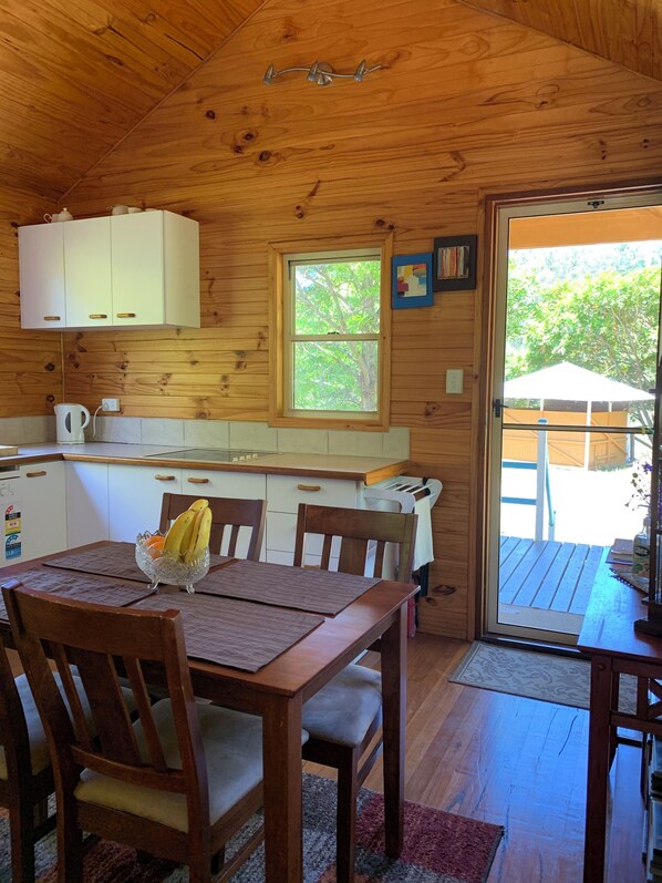 A wooden cabin interior with a dining table, chairs, a window, and a view of the outdoors.