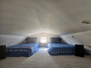 Un pequeño dormitorio en el ático con dos camas, una ventana y techo inclinado.