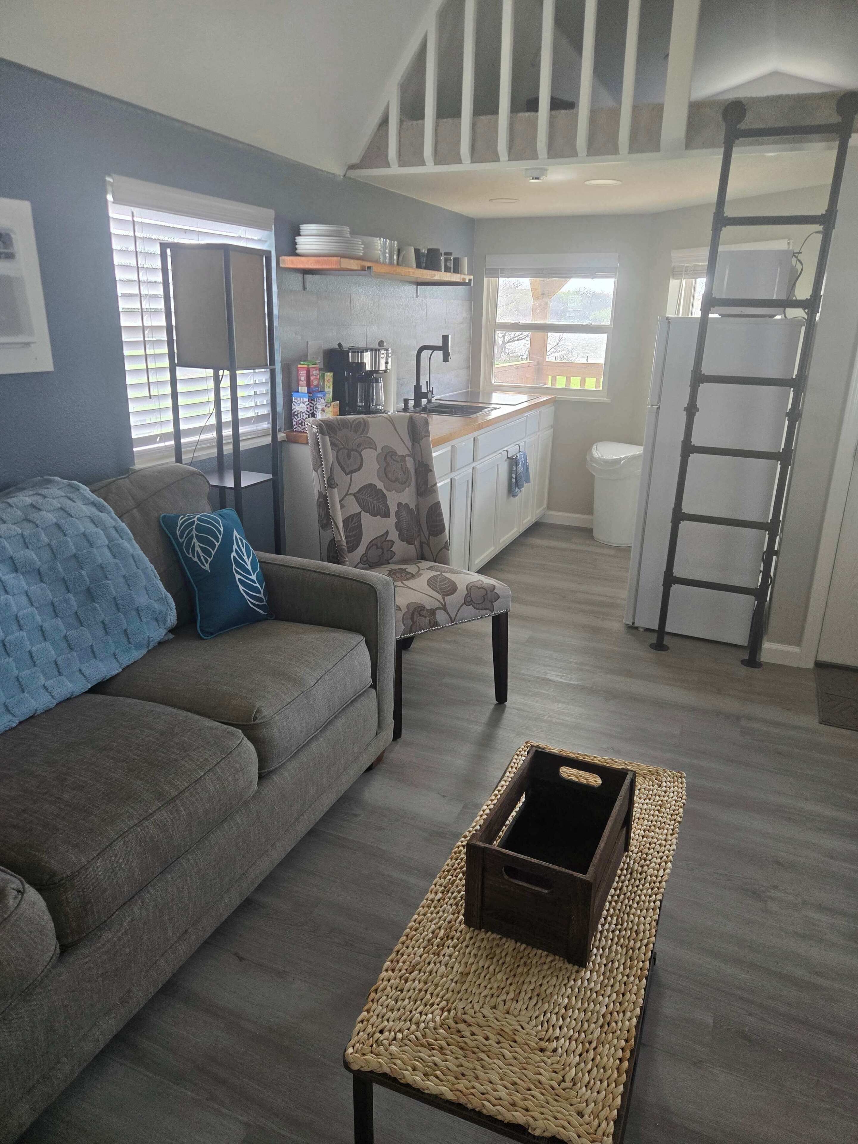 Sala de estar con sofá, sillón, mesa de centro, zona de cocina con pileta y una escalera.