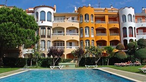 Una piscina con sillones de descanso y un edificio con varios balcones.