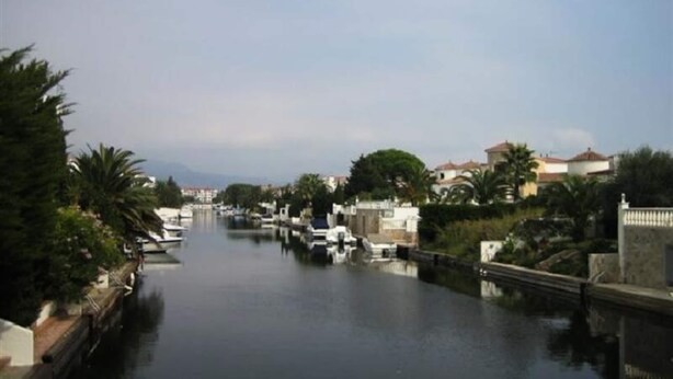 Un canal con barcos, rodeado de vegetación y edificios.