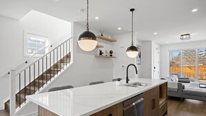 Cozinha moderna com ilha central, lava-louças embutida e iluminação pendente.