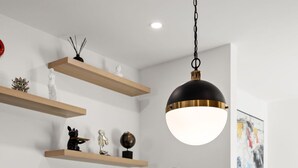 Uma cozinha moderna com bancada branca, pia de aço inoxidável e torneira preta. Há prateleiras de madeira acima do balcão com objetos decorativos.