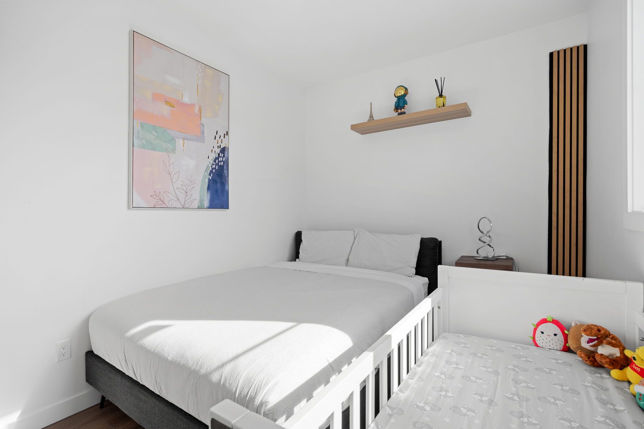 Ein Schlafzimmer mit einem Bett, einem an der Wand befestigten Regal mit Figuren, einem Zierkissen und einem Wandbild.