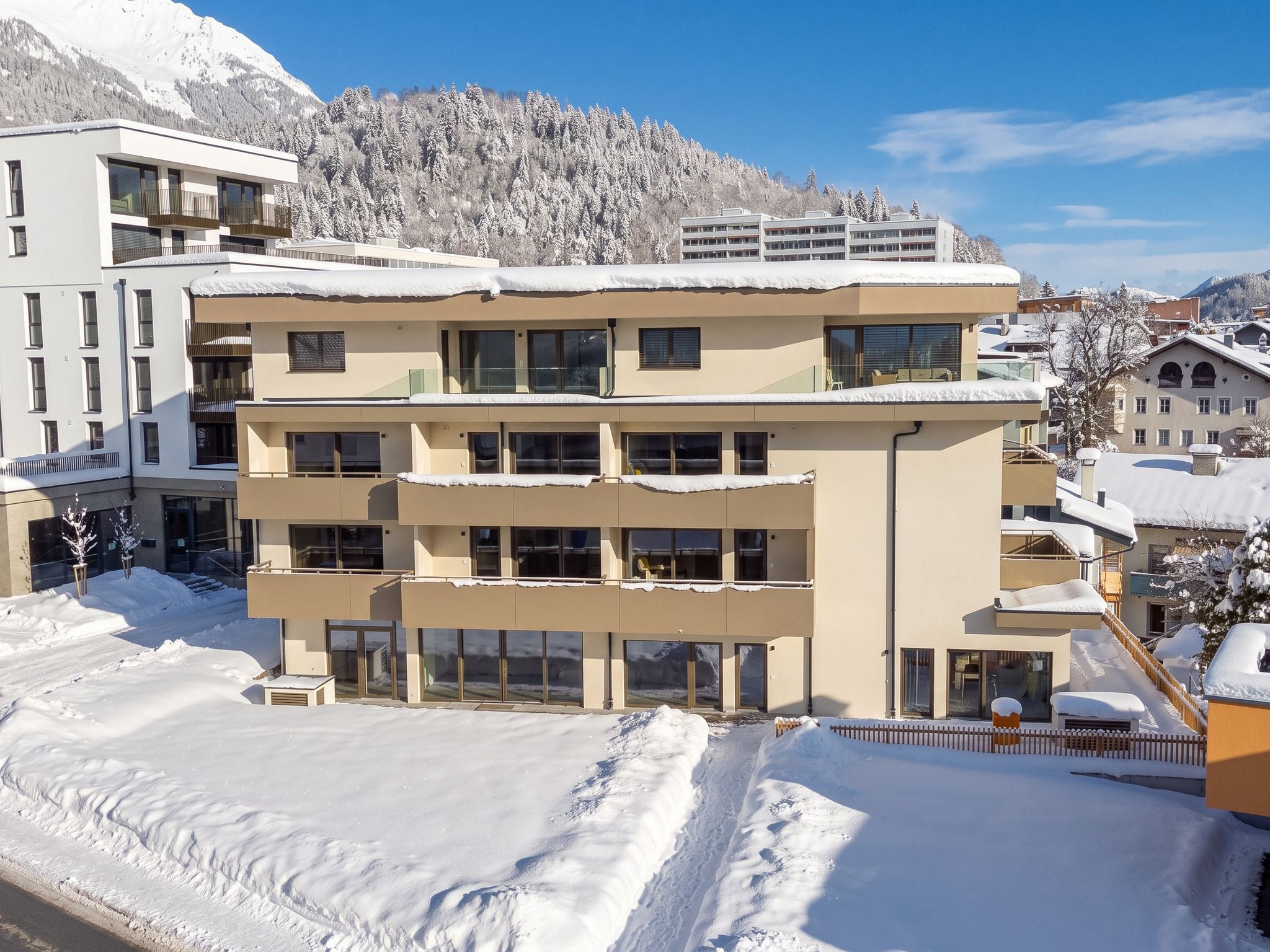 Un hotel de varios pisos con balcones y ventanas amplias, rodeado de árboles nevados y montañas.