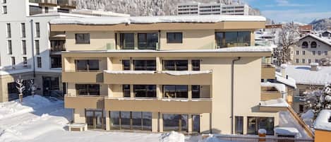 A multi-story hotel with balconies and large windows, surrounded by snow-covered trees and mountains.