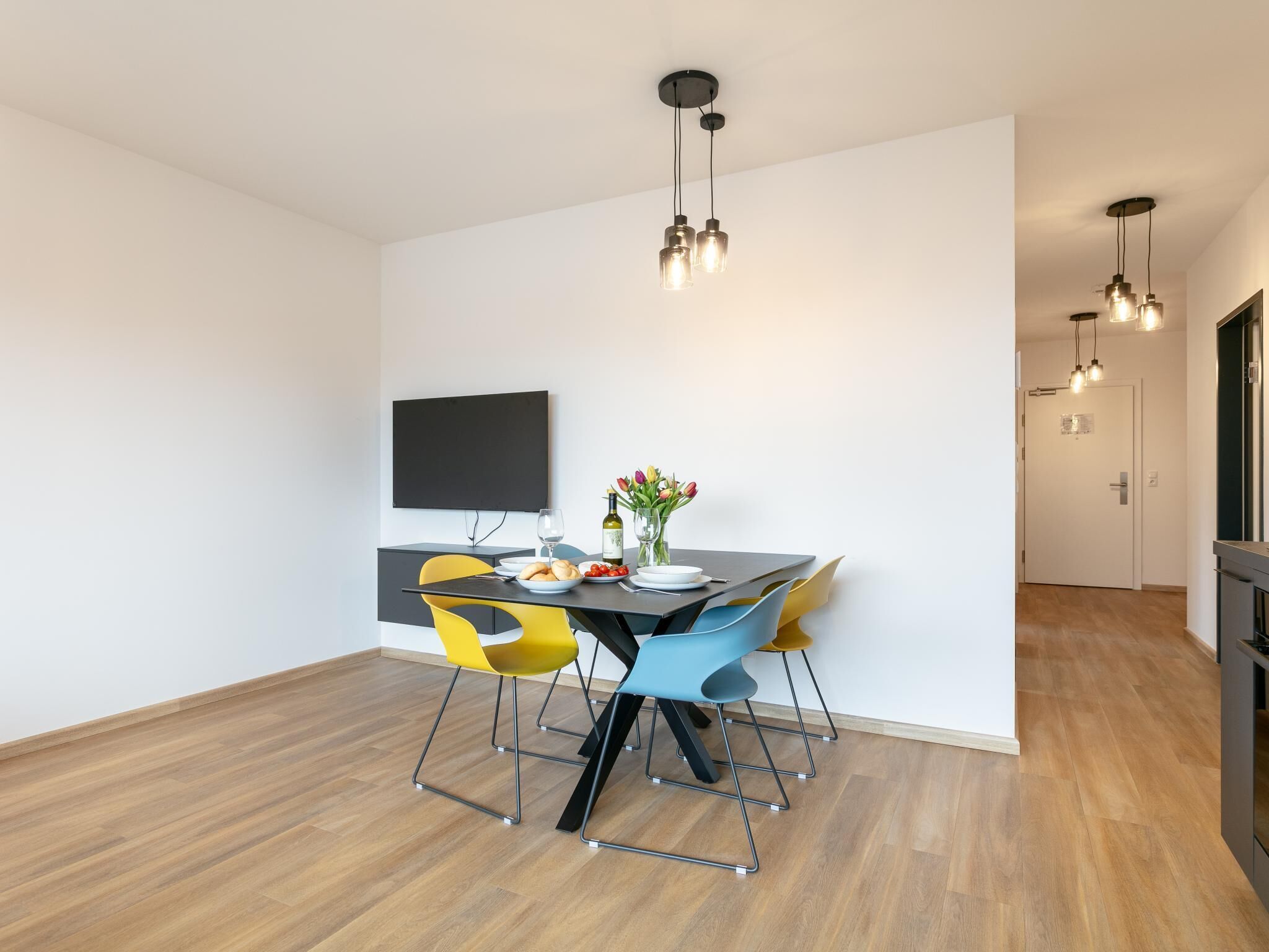 Un espace repas moderne doté d’un téléviseur à écran plat, d’une table mise avec des assiettes, des verres et un vase de fleurs.