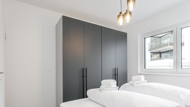 A modern hotel room with a large wardrobe, a bed with white linens, and a view of the outside. - Stylish holiday apartment in Jenbach centre (Jenbach)