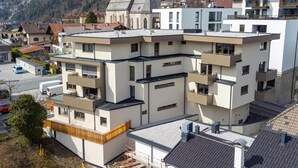 A multi-story building with balconies, a church with a clock tower, and a mountainous backdrop. - Stylish holiday apartment in Jenbach centre (Jenbach)