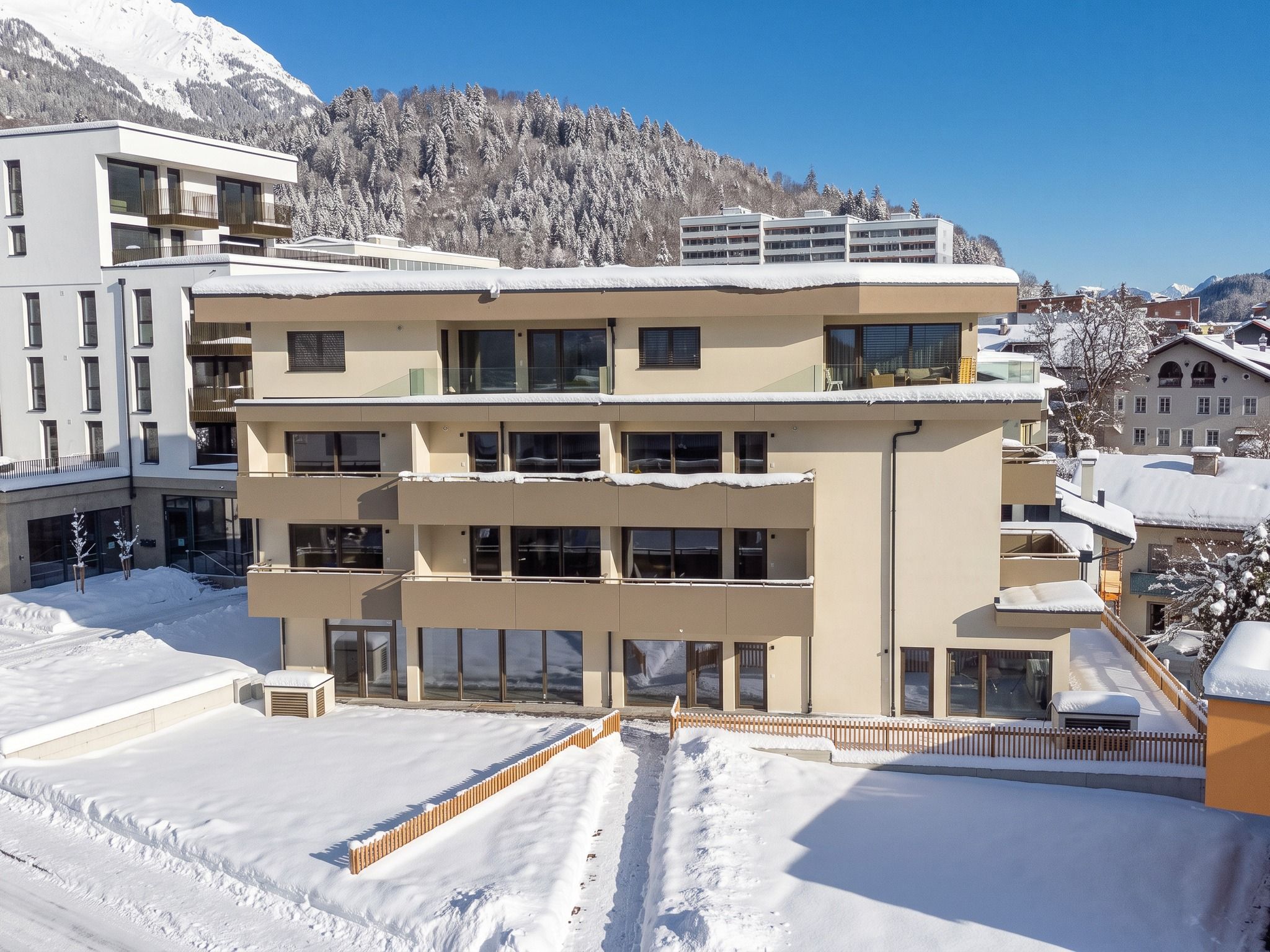 A multi-story hotel with balconies, a snow-covered parking area, and a mountainous backdrop.