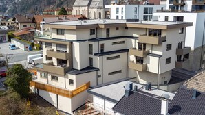 Ein mehrgeschossiges Gebäude mit Balkonen, ein Kirchengebäude mit einem Glockenturm und Wohnhäuser im Hintergrund.