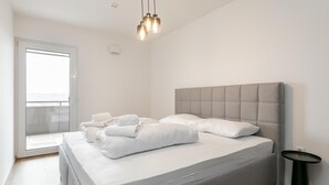 Ein modernes Schlafzimmer mit einem großen Bett, einem kleinen runden Tisch und einem Balkon mit Blick.
