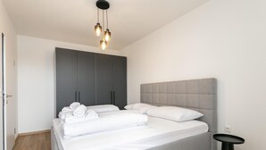 Una camera da letto moderna con un letto grigio, lenzuola bianche, una testata grigia e un comodino nero.