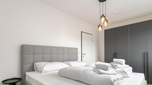 Ein modernes Schlafzimmer mit einem großen Bett, einem grauen Kopfteil und einem Nachttisch.