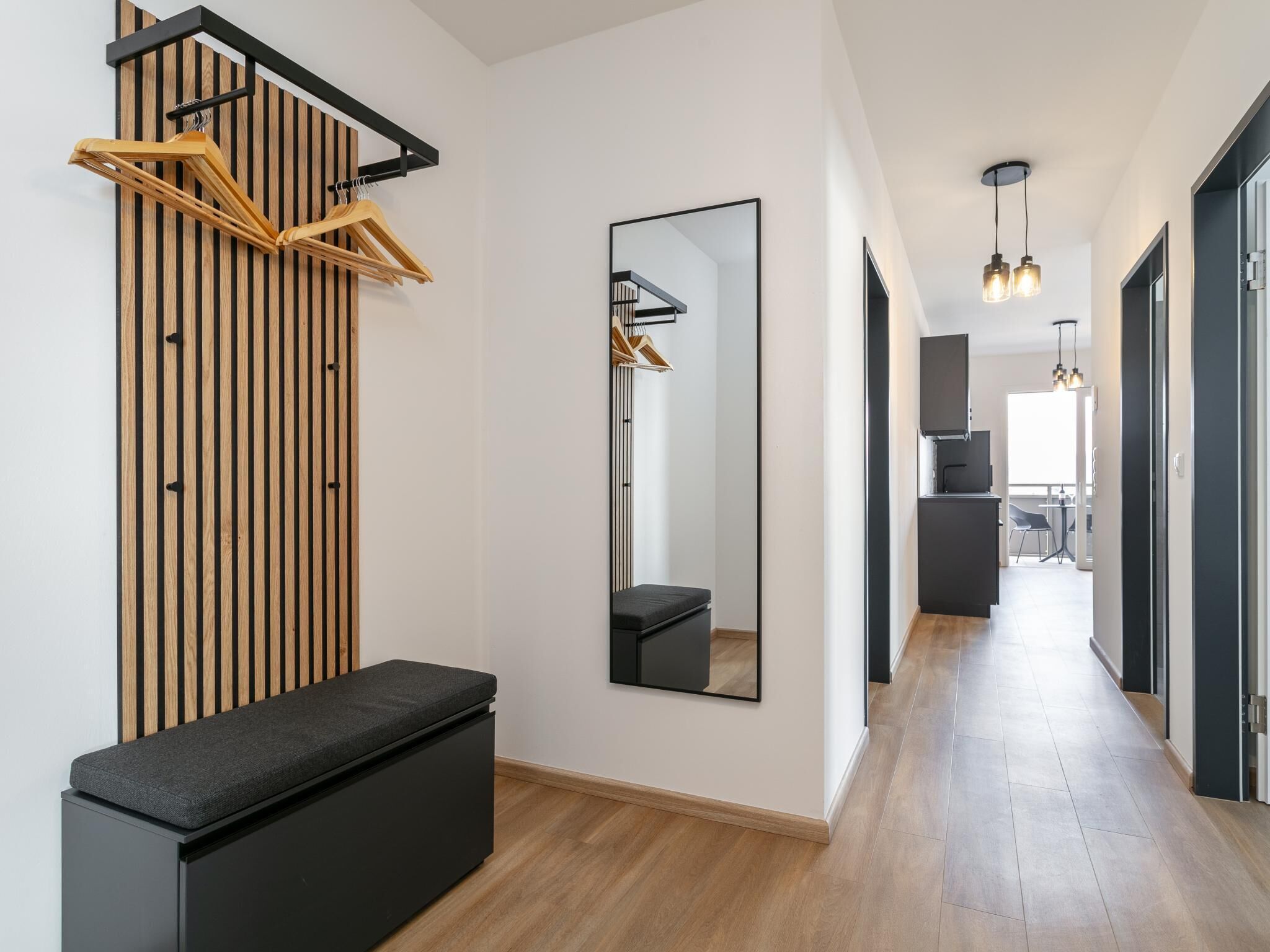 Ein moderner Flur mit einer Bank, einer Wand aus Holzlamellen, einem Spiegel und Pendelleuchten.