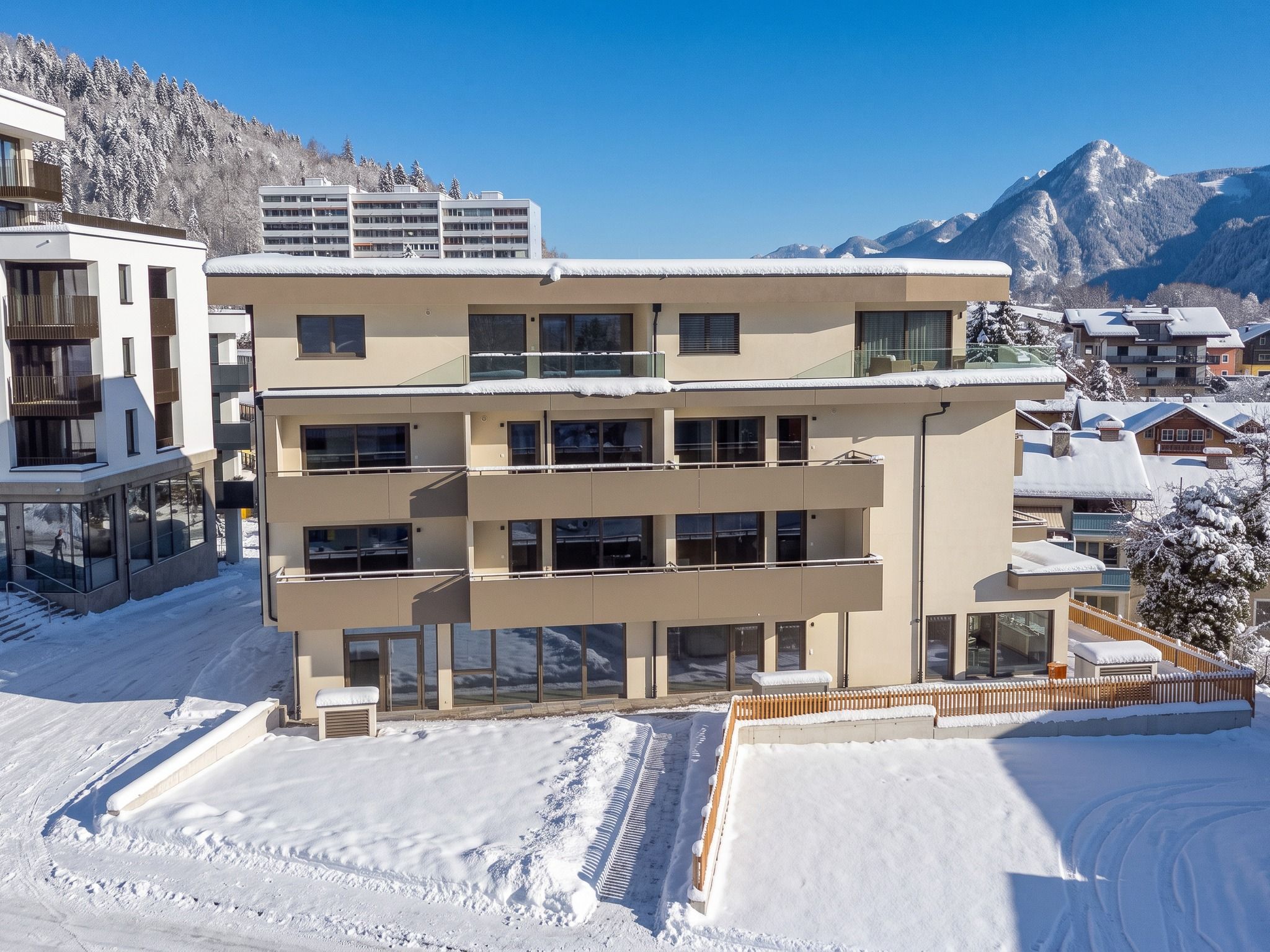 Een hotel met meerdere verdiepingen, balkons, grote ramen en een besneeerd landschap met bergen op de achtergrond.