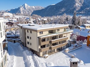 Un edificio de varios pisos con balcones, rodeado de árboles nevados y montañas al fondo.